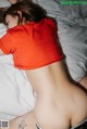 A woman laying on top of a bed in a red shirt.