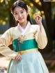 A woman in a green and yellow hanbok poses for a picture.