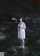 A woman in a white dress standing on a rock in the water.