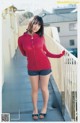 A woman in a red hoodie and shorts posing on a balcony.