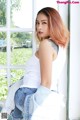 A woman sitting on a window sill wearing a white tank top and jeans.