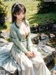 A woman in a white dress sitting on a rock by a pond.