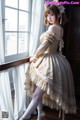 A woman in a dress standing by a window.