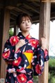 A woman in a kimono leaning against a wooden pole.