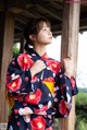 A woman in a kimono leaning against a wooden pole.