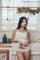 A woman in a white tank top and panties standing in a kitchen.