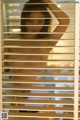 A naked woman standing in front of a window with blinds.